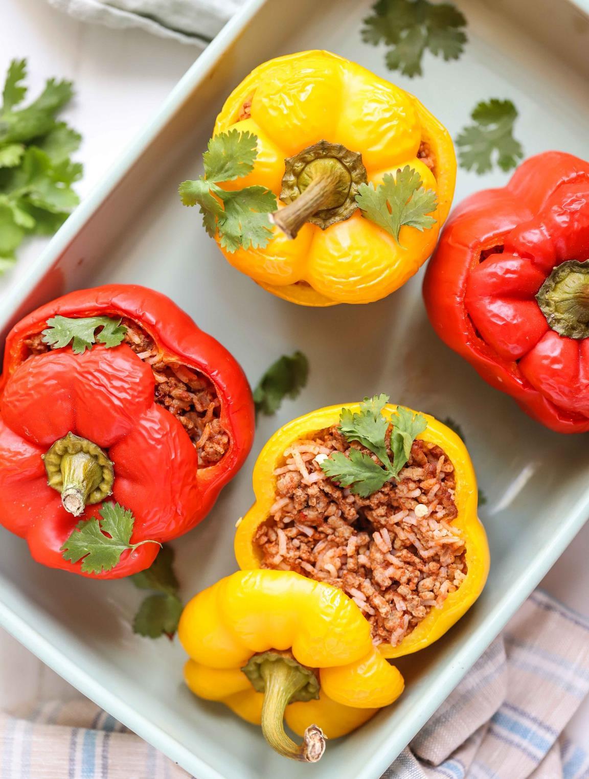 Four Mexican stuffed bell peppers filled with seasoned beef and rice, baked until tender in a ceramic dish