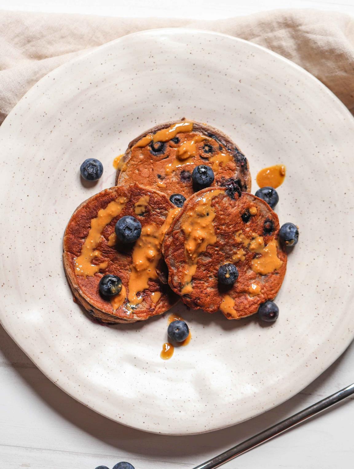 A high protein blueberry pancake topped with fresh blueberries, served on a white plate