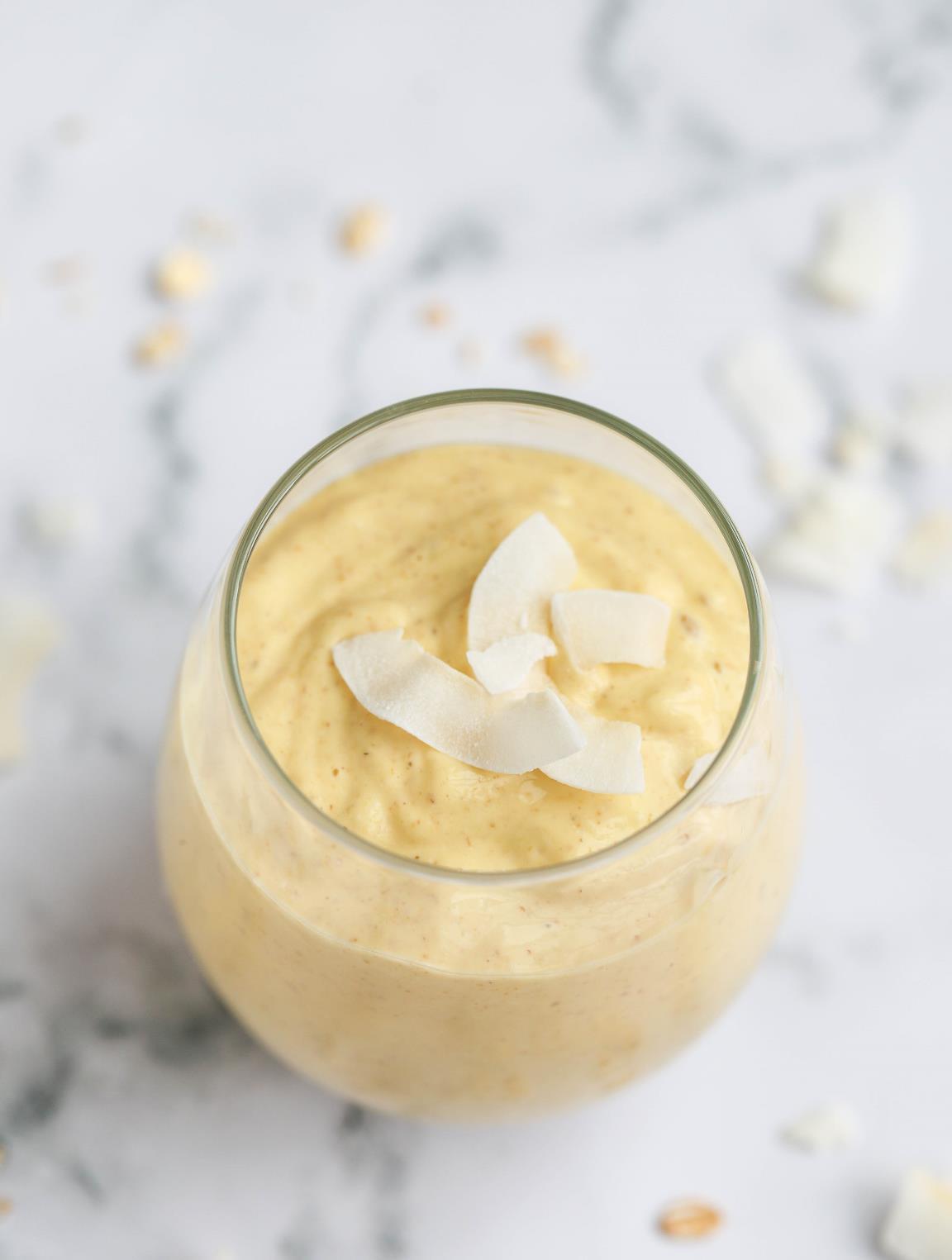 Two glasses of pina colada smoothie with pineapple chunks and desiccated coconut on the side