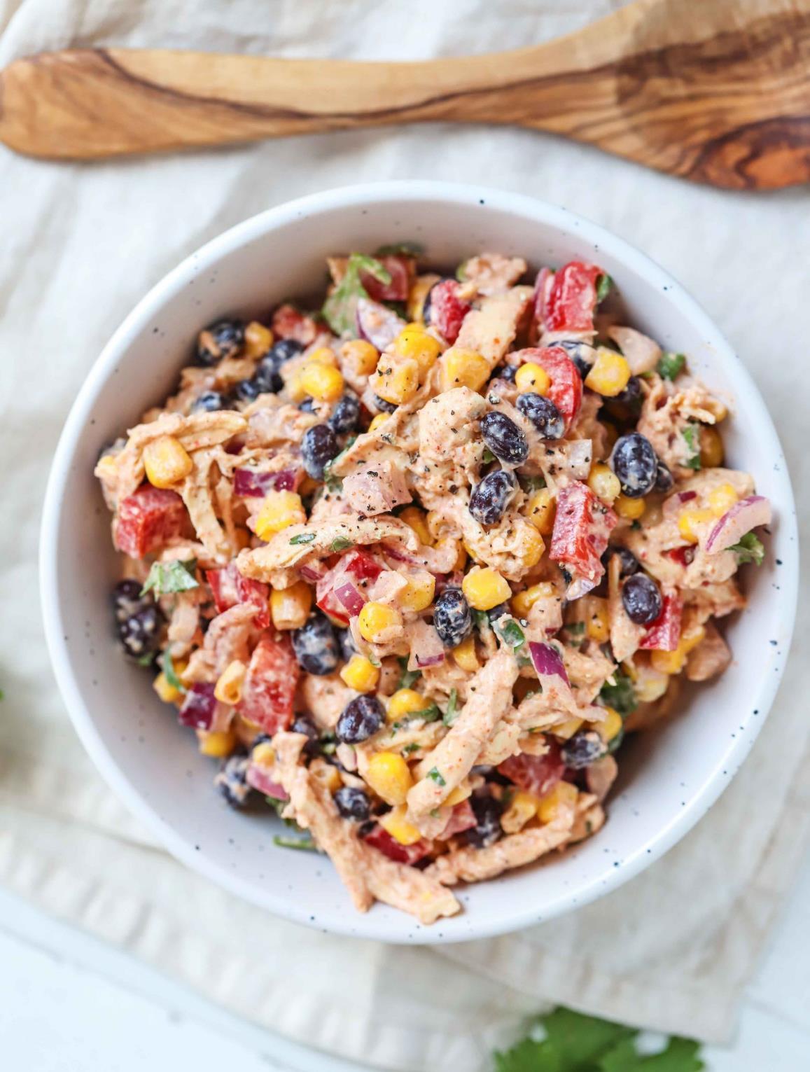 A bowl of southwest chicken salad with shredded chicken, black beans, sweet corn and red pepper in a creamy sriracha lime dressing